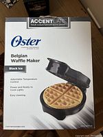 Front view of Oster Belgian Waffle Maker box showing product branding, model, and features including adjustable temperature control and easy cleaning.