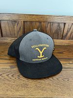 Front view of the Yellowstone Dutton Ranch hat showing the embroidered logo and text in yellow on grey fabric with a black brim.