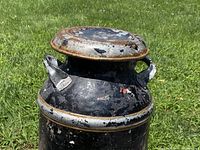 Close-up photo of top part of the black and silver metal milk can, showing the lid, handles, and rust spots.