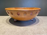 Front side view of wooden Baribocraft salad bowl with oval cutouts and three small painted feet, displayed on grey surface with dark background.