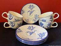 Front view of four teacups stacked next to four matching saucers against red background showing blue floral patterns and detailing.