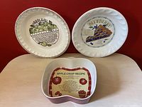 Blueberry and apple pie ceramic plates and an apple crisp ceramic dish arranged on a wooden surface with a red wall background.