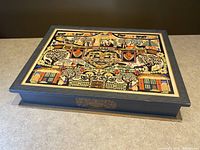 Top view showing colorful folk art collage on box lid featuring trees, buildings, and patterned motifs.