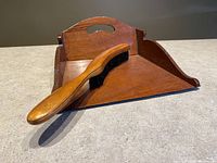 Edwardian style wooden crumb tray with a cut-out handle and curved edges, shown with the matching brush placed inside on the tray surface.