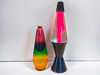 Two lava lamp inserts: one rainbow-colored bottle with a metal cap and one bottle with pink wax; and a black-base lava lamp with pink wax in clear liquid.