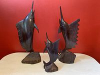 Front view of three ironwood marlin swordfish carvings on a table against a red wall.