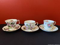 Front view of three floral teacup and saucer sets with red backdrop