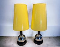 Front view of both lamps showing chrome ball bases and tall glossy yellow tapered shades