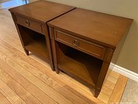Pair of vintage Canadian nightstands with one drawer and an open shelf, medium brown wood finish, carved leaf details, metal ring drawer pulls.