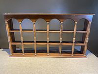 Front view of the wooden plate display shelf rack showing carved vertical supports and two horizontal rails for plate display.