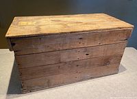 Front view of a primitive wooden crate showing multiple horizontal slats forming the body and top surface.