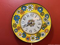 Front view of the retro yellow tin plate daisy clock showing the flower pattern and clock face.