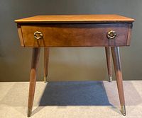 Front view of walnut standing table with single drawer and tapered legs with brass caps.