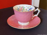 Pink Aynsley porcelain teacup on matching saucer showing exterior and gold trim.