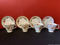 Four Royal Albert teacups with matching saucers, all decorated with pink rose floral patterns, gold rims, and ornate handles, displayed against a red background.