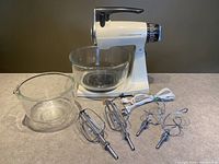 Front view of Sunbeam Mixmaster stand mixer with two clear glass bowls and four metal beaters set in front, all items clean and in good condition.