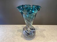 Front view of a twisted stripe pattern ruffled glass vase with green and purple hues on a neutral background.