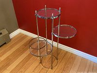 Front view of the vintage brass tiered plant stand showing its three tiered circular glass platforms and brass frame.