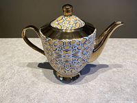 Front and side view of gold-trimmed tea pot with wildcat pattern resembling leopard or cheetah spots, showing intricate animal print and shiny metallic gold elements