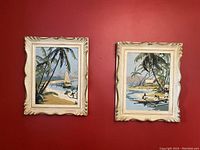 Two vintage island paintings with palm trees and sailboat/figures in ornate gold frames against red wall