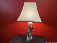 Front view of vintage ceramic flower lamp with fabric lampshade against red wall.