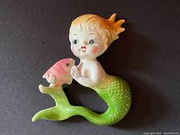 Image showing the front view of the vintage Norcrest ceramic mermaid wall plaque holding a pink angel fish, on a black background.