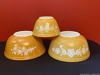 Three Pyrex Butterfly Gold bowls, two model 403 and one model 401, arranged upside down showing exterior floral pattern and bowl bottoms.