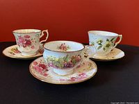 Three vintage floral teacups placed on matching saucers shown against a red background