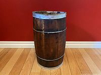 Side view of vintage wooden barrel keg standing on wooden floor against red wall.