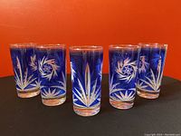 Five cobalt blue vintage glasses with white etched atomic pinwheel design arranged in a semi-circle on orange background.