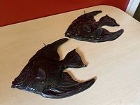 Two dark metal angel fish wall hangings on a light wood table showing size and condition.