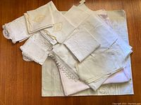 Varied pile of six vintage pillow cases, some embroidered, and tablecloths in soft colors.