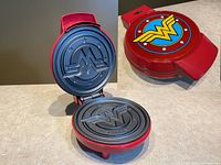 Open view of Wonder Woman waffle maker showing interior non-stick plates with Wonder Woman logo and star design embossed.