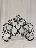 Front view of black spiral wine bottle holder showing eight circular wine slots and decorative swirl detailing at top.