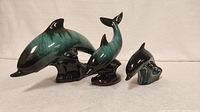 Frontal view of three Blue Mountain pottery dolphin figurines in green and black glaze, showing size differences.