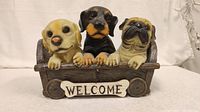 Front view of three dog figurines (Labrador, Rottweiler, Pug) on a wooden cart with 'WELCOME' plaque