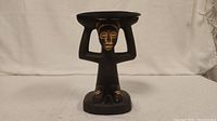 Front view of a dark wooden carved figure kneeling and holding a circular tray above its head with detailed facial and body carvings.