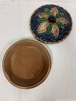 Top and bottom view of the blueberry pie ceramic dish showing the lid with blueberry and leaf motif and plain brown base.