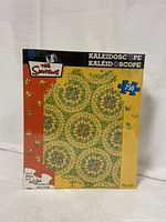 Box front view showing vibrant kaleidoscope circular pattern with The Simpsons logo and 750 piece count.