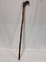 Full-length view of the wooden cane standing upright against a plain background showing overall form and carved shaft.