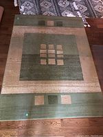 Full view of the rectangular Odessa area rug laid on wooden flooring showing geometric pattern and color tones of green, beige and taupe.