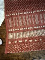 Close-up of the rug edge showing woven pattern and wear, reddish brown with cream detailing.