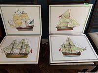 Four framed maritime art prints showing various types of sailing ships with full sails, arranged in a two by two grid on a sofa.