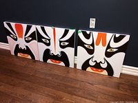 Three square triptych prints side by side on floor against wall showing stylized Asian face images with bold black, white, orange colors