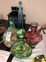 Four glass bottles filled with used wine corks, green, clear, purple, and tall blue bottle visible with size stickers on each