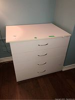 Front view of the white melamine cabinet showing four drawers with metal handles and signs of wear.