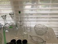 Three crystal decanters with stoppers, one without stopper, pinwheel crystal bowl, cream and sugar set, oval serving dish, two wine serving bottles on windowsill.