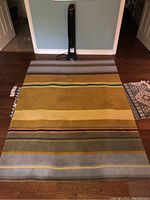 Full view of Ikea Stockholm wool rug laid out flat on hardwood floor, showing striped pattern with mustard yellow as dominant color
