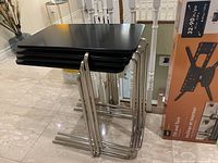 Image showing stacked four black lacquered top nesting tables with chrome tubular metal frames.