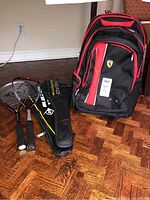 Photo showing two squash racquets on the floor with one black cover, next to a Ferrari branded black and red sportsbag.